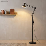 Black swing arm floor lamp beside a wall shelf casting warm light on a rug