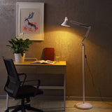 White adjustable floor lamp arched over a wooden desk and open book