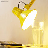 Yellow cone metal shade with side vent slots glowing above a glass of water