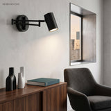Black swing arm sconce lit above a sideboard and framed mirror