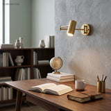 Gold swing arm sconce lit above a desk with books and a globe