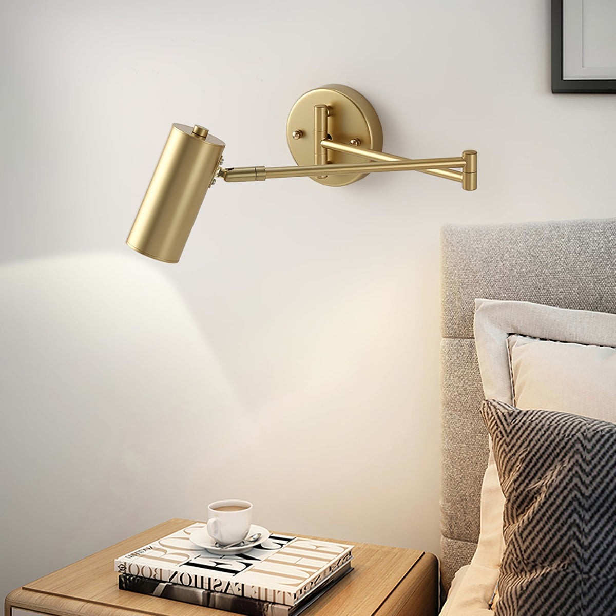 Gold swing arm sconce lit above a bedside table and coffee cup