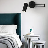 Black swing arm sconce lit beside a green upholstered headboard