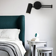 Black swing arm sconce lit beside a green upholstered headboard