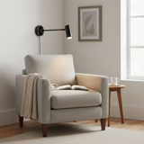 Black swing arm sconce lit beside an armchair and side table