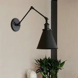 Black swing arm sconce beside a dark post and a potted plant