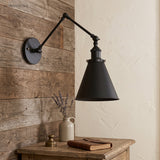 Black swing arm sconce on timber boards above a small writing desk
