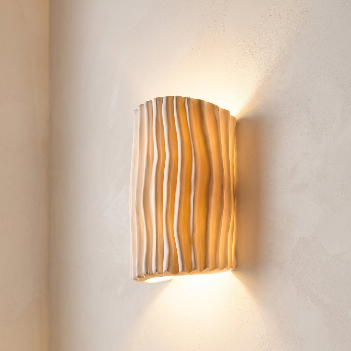 Lit cream striped half cylinder resin wall sconce on pale plaster wall