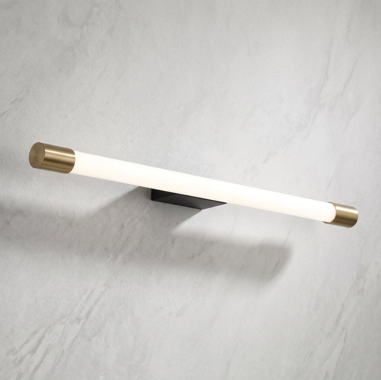 Slim aluminum tube LED wall sconce with brass end caps on a marble wall