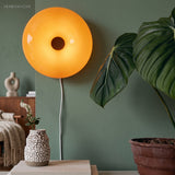 Amber donut glass lamp on a console by a green wall