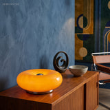 Amber donut glass lamp on a console by a blue wall