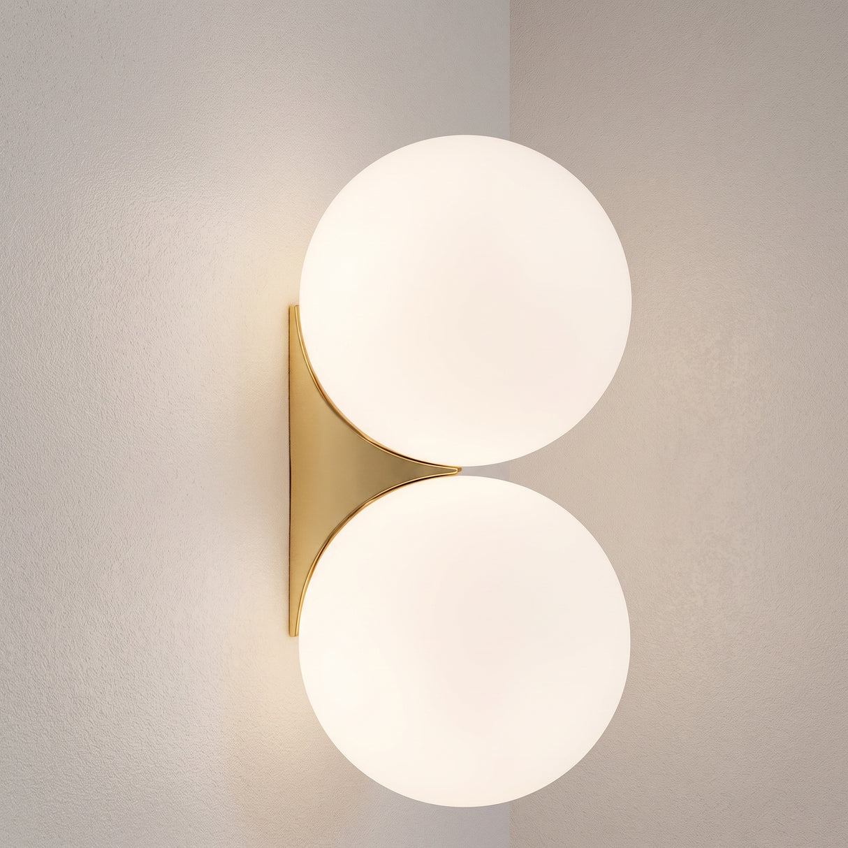 Double frosted glass globe wall lamp with gold bracket on a plain wall