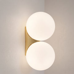 Double frosted glass globe wall lamp with gold bracket on a plain wall