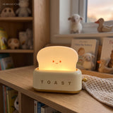 Cream toaster table lamp on a kids bookshelf beside soft toys