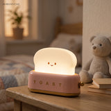 Pink toaster table lamp lit beside a teddy bear in a nursery