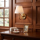 Warm brass pleated linen sconce on walnut panelling above a desk