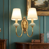Two light gold sconce with white fabric shades on a green wall