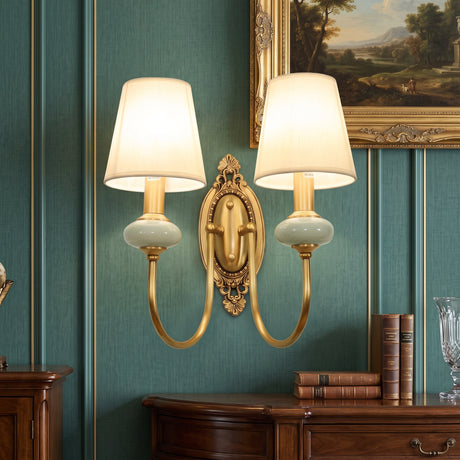 Two light gold sconce with white fabric shades on a green wall
