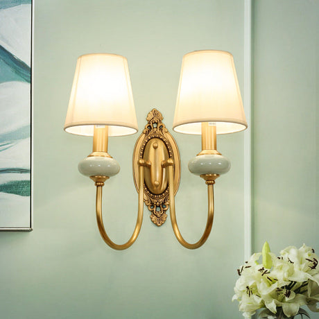 Two light gold sconce on a green wall above white lilies