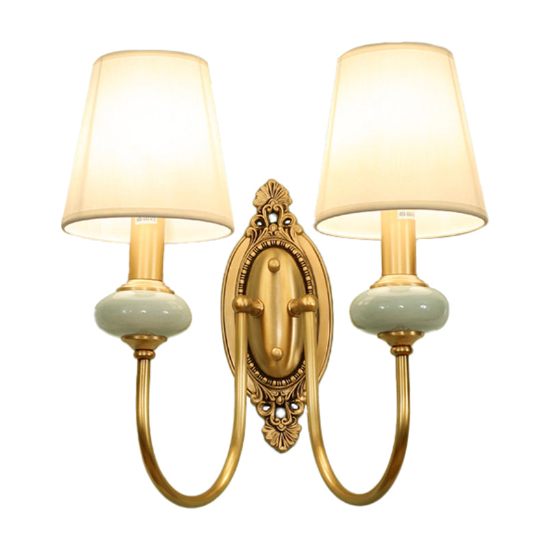 Two light gold sconce with both shades lit on plain white