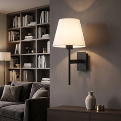 Wall sconce with a white tapered fabric shade on a black bracket beside a sideboard