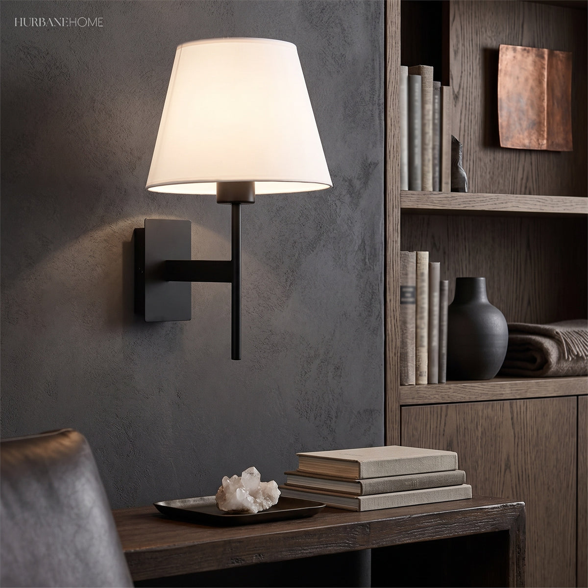 Wall sconce beside open shelving above a desk with books and a vase