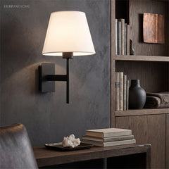 Wall sconce beside open shelving above a desk with books and a vase