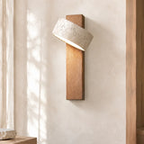 Travertine shade tilted upward on a wood arm against a sunlit plaster wall