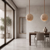 Pair of travertine ball pendants above a dining table by tall windows
