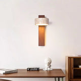 Walnut wall sconce with travertine shade above a desk and small white figurine