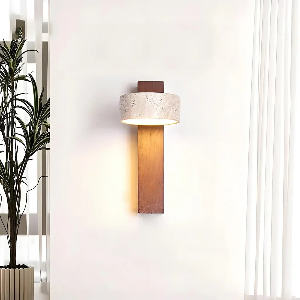 Travertine wall sconce casting a warm downward glow beside a tall potted plant