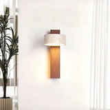 Travertine wall sconce casting a warm downward glow beside a tall potted plant