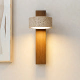 Wood wall sconce with upright travertine drum shade beside a framed print
