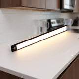Black LED bar lighting a white kitchen counter from under a cabinet