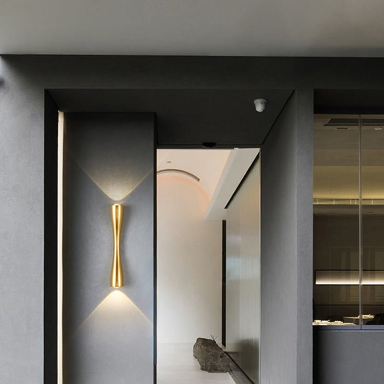 Gold slim wall light lit in a narrow corridor with a stone floor