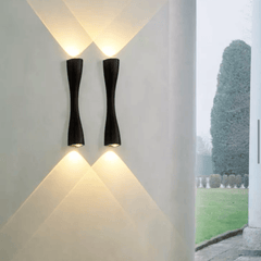 Two black slim wall lights lit on a rendered garden wall