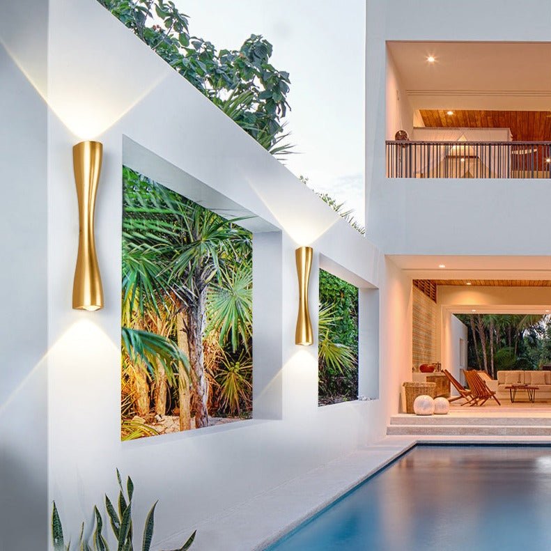 Gold slim wall lights lit on a white wall beside a swimming pool