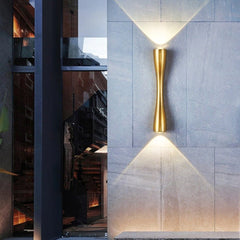 Gold slim wall light lit on a large stone tiled entrance wall