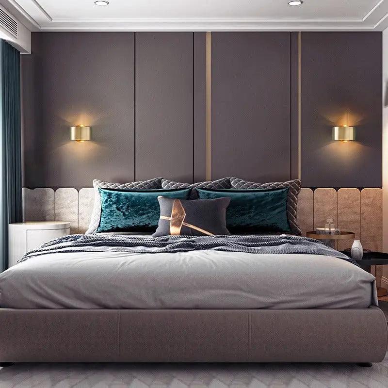 Gold sconces mounted either side of an upholstered bed headboard
