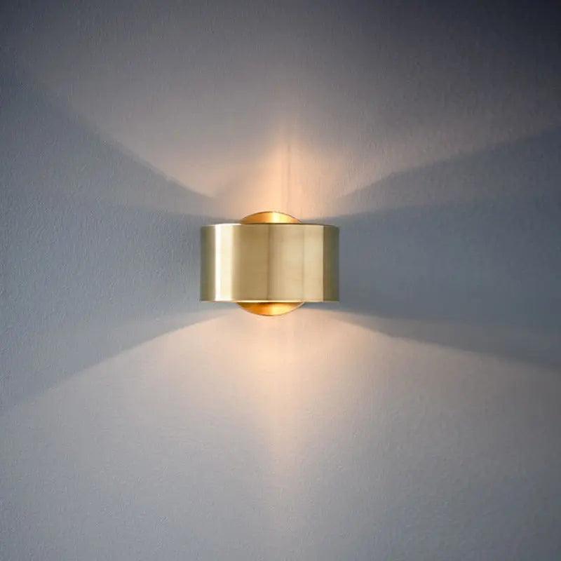 Gold sconce lit on a pale wall with a wide upward light spread