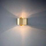 Gold sconce lit on a pale wall with a wide upward light spread