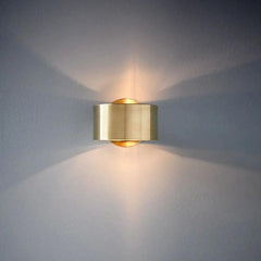 Gold sconce lit on a pale wall with a wide upward light spread
