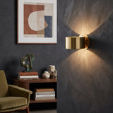 Gold curved wall sconce throwing light up and down a dark wall