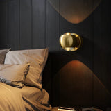 Gold orb sconce lit above a bed with linen pillows and dark panelling