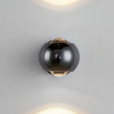 Black orb sconce lit on a plain white wall with beams above and below