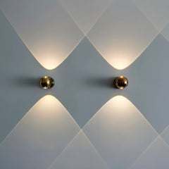 Two gold orb sconces lit side by side on a soft blue wall