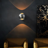 Chrome orb sconce lit on a black wall beside marble artwork