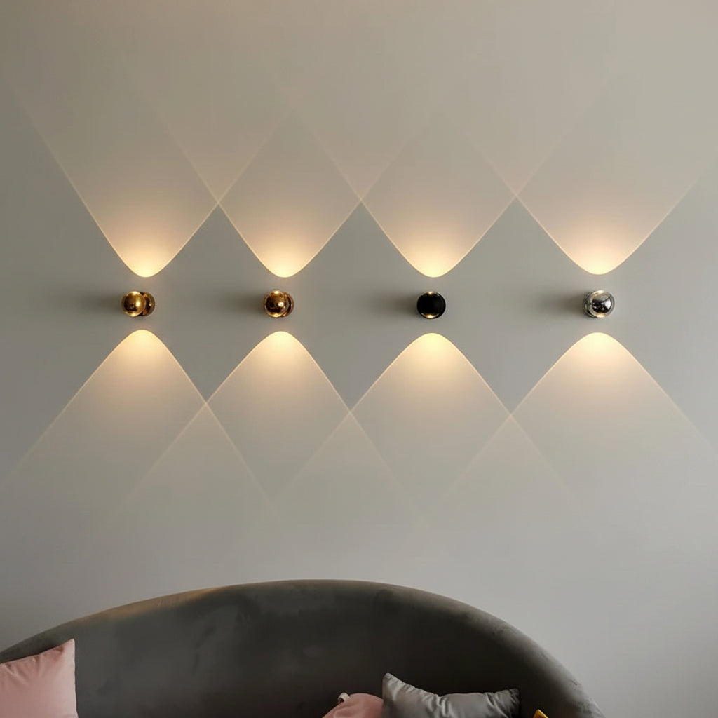 Row of four orb sconces in gold black and chrome lit on a pale wall