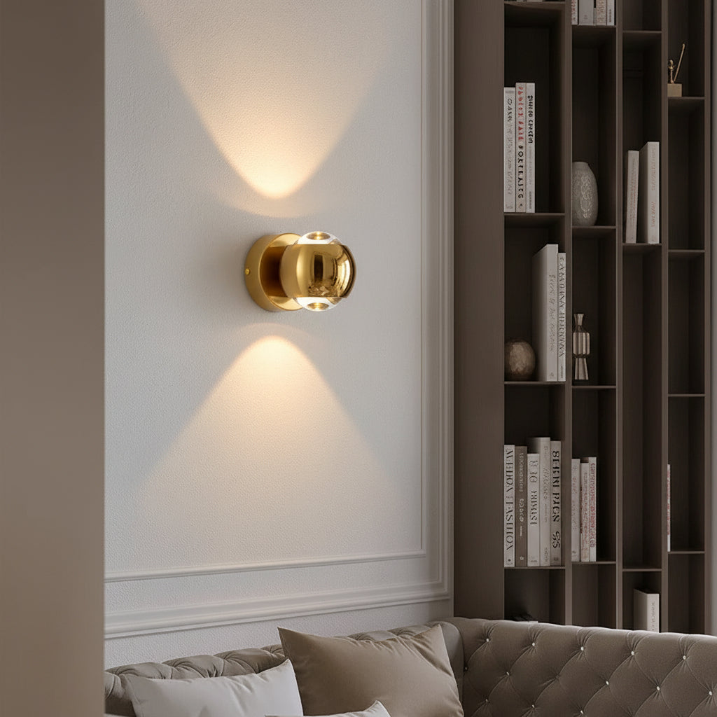 Gold orb sconce lit on a pale wall beside dark shelving and a sofa