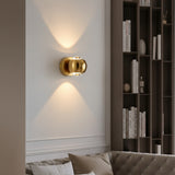 Gold orb sconce lit on a pale wall beside dark shelving and a sofa